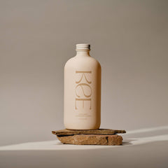 A beige KEE Liquid Marine Collagen - Limoncello bottle stands on stones, highlighting marine collagen in a neutral setting.