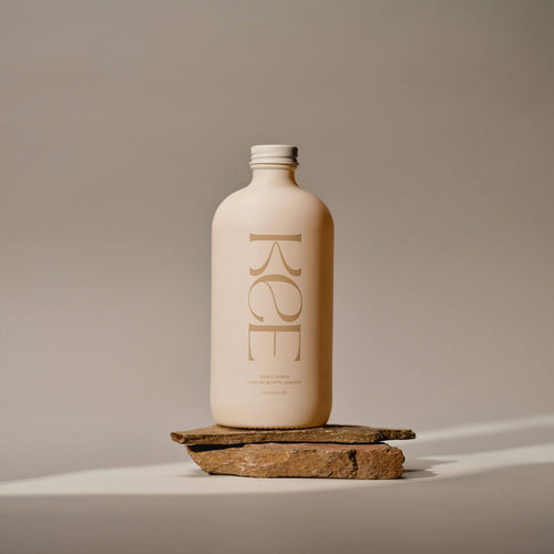 A beige KEE Liquid Marine Collagen - Limoncello bottle stands on stones, highlighting marine collagen in a neutral setting.