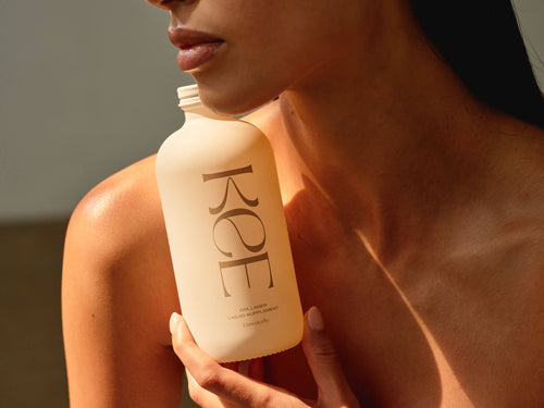 Woman holding a frosted bottle of KEE Liquid Marine Collagen - Limoncello near her face and collarbone.