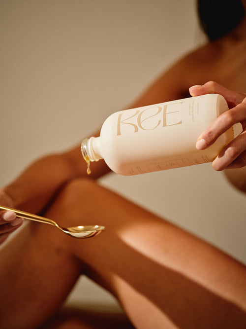 Someone pours KEE Liquid Marine Collagen - Limoncello into a gold spoon, with legs visible in the background.