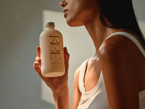 A woman in a white tank top holds a KEE Liquid Marine Collagen - Limoncello bottle, highlighting its benefits.