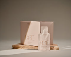 A KEE Liquid Marine Collagen Sachet - Limoncello is displayed before its box on a stone slab in soft, natural light.
