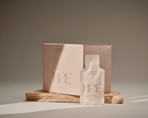 A KEE Liquid Marine Collagen Sachet - Limoncello is displayed before its box on a stone slab in soft, natural light.