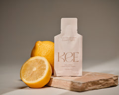 A lemon and a half sit next to a KEE Liquid Marine Collagen Sachet - Limoncello on a stone slab.