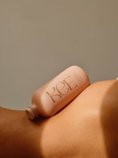 A pink KEE Liquid Marine Collagen - Mango Sorbet bottle rests on a persons bare back against a neutral background.