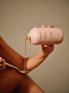 A hand pours KEE Liquid Marine Collagen - Mango Sorbet from a pink bottle into a gold spoon against a neutral background.