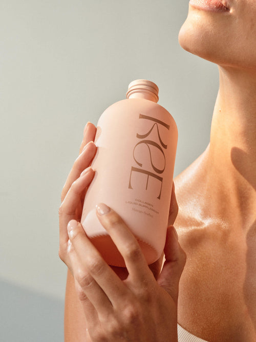 A person holds a KEE Liquid Marine Collagen - Mango Sorbet bottle near their face, skin glowing in soft light.