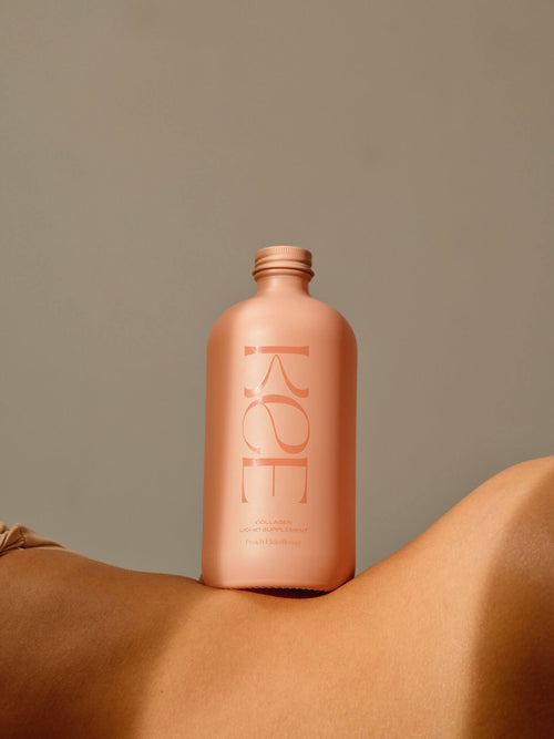 A pink KEE bottle of Liquid Marine Collagen - Peach Elderflower on bare skin, set against a plain beige background.