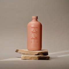A matte pink bottle labeled KEE—Liquid Marine Collagen - Peach Elderflower—stands on stacked flat stones.