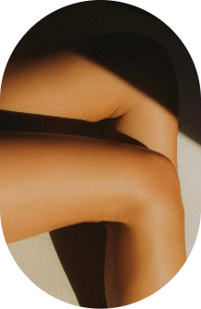 Close-up of crossed bare legs in sunlight and shadow on a light background.