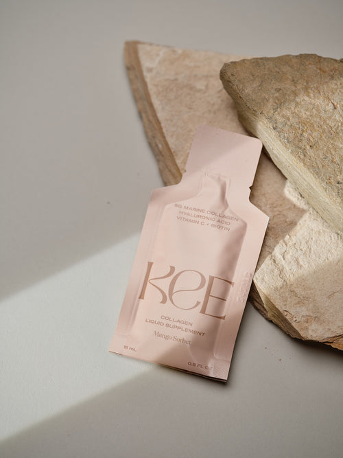 A KEE Liquid Marine Collagen Sachet - Mango Sorbet sits on beige stone slabs against a light background.
