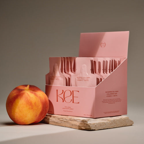 A peach sits beside a pink KEE Liquid Marine Collagen Sachet - Peach Elderflower box on a stone slab.